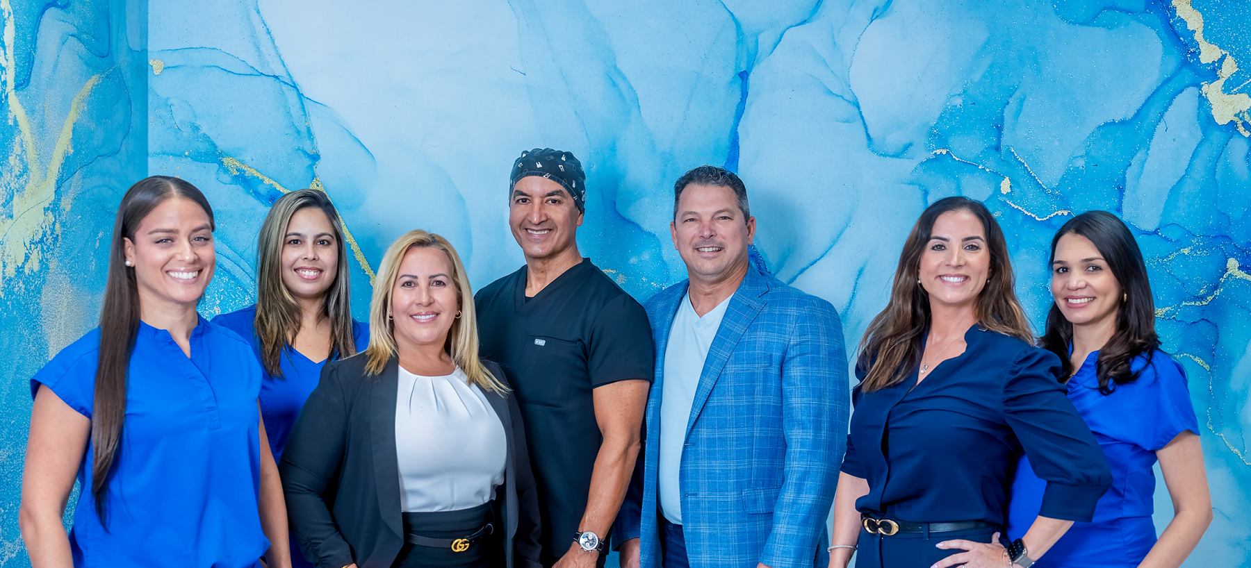 El equipo de Estelar Dental, sonriendo, ante la pared azul de la clínica.